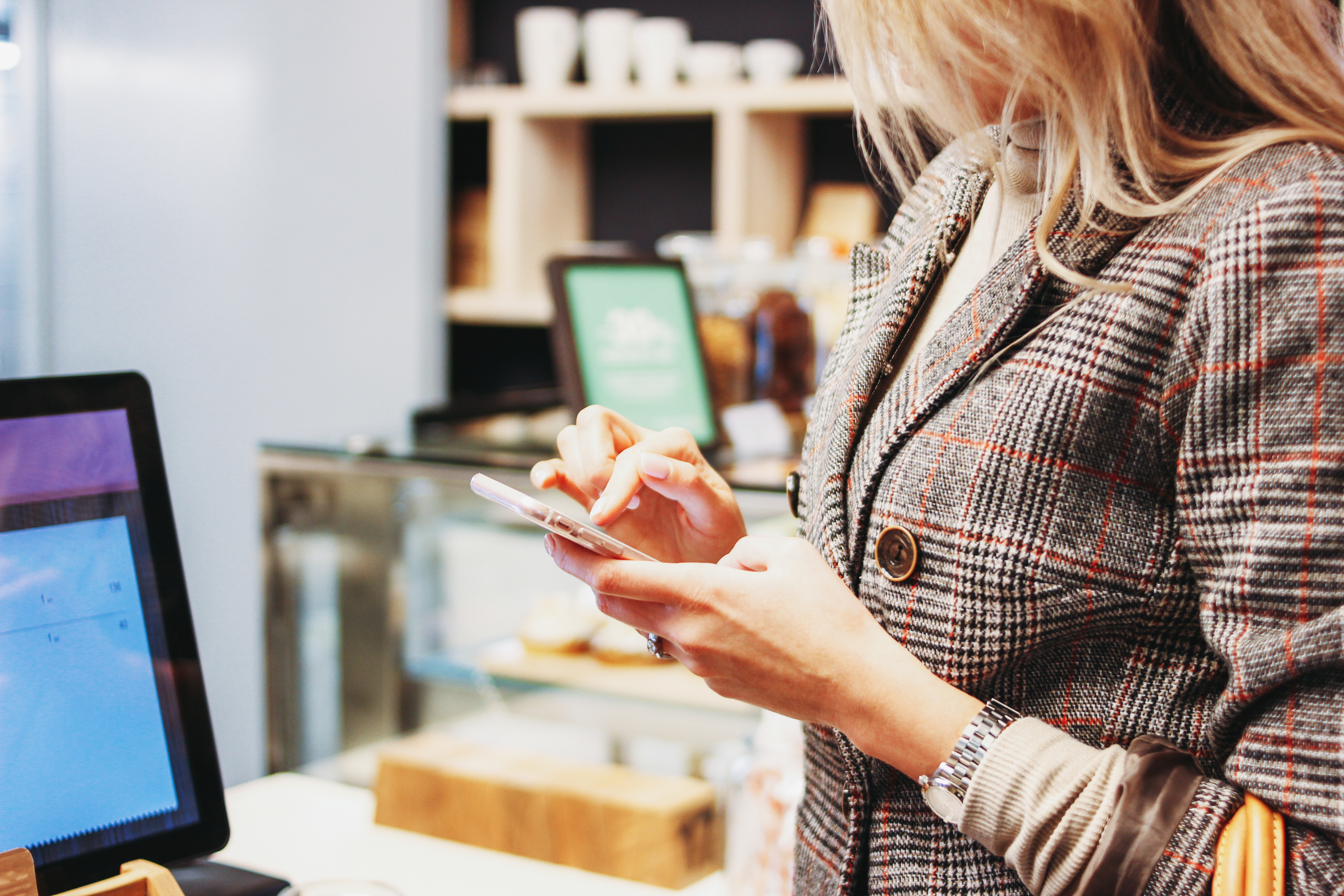 Young woman with mobile phone in hands pays for order at checkout in shop